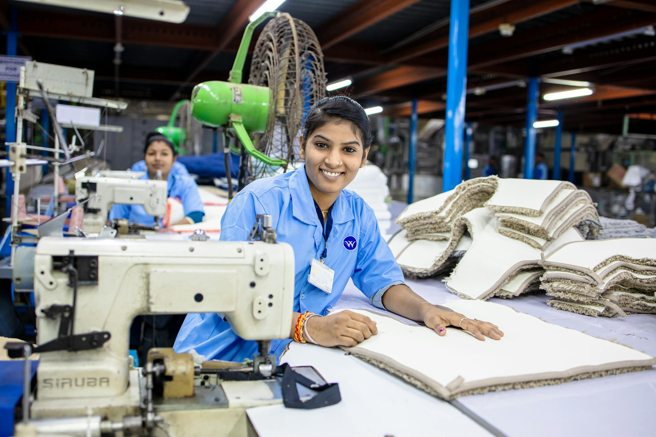 South Asian woman smiling at fabric factory workstation with sewing machine.